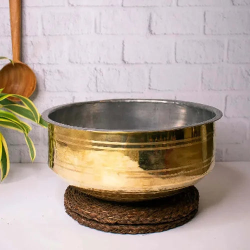 Brass Cooking Pot Sarva Kadai on a woven stand with a white brick wall background-Zishta Traditional Cookware