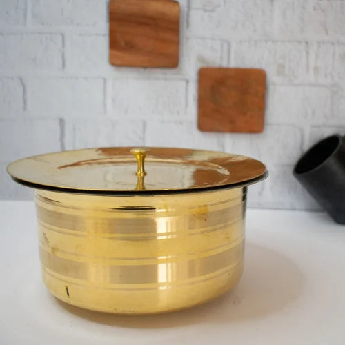 Brass Patila with a lid on a white surface with a light gray textured wall in the background-Zishta Traditional Cookware