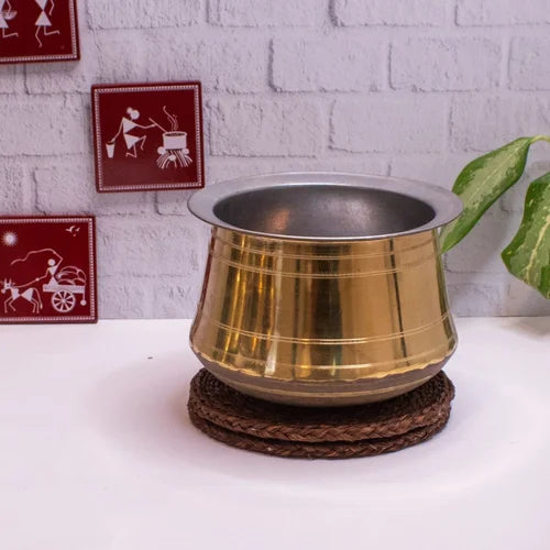 Brass Rice pot on a woven stand with decorative wall art in the background-Zishta Traditional Cookware