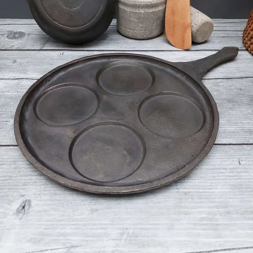 Cast iron mini uthappam pan with four circular depressions on a wooden surface-Zishta Traditional Cookware
