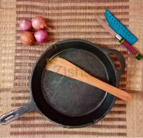 Cast iron skillet with wooden spatula, knife, and onions on a woven mat-Zishta Traditional Cookware