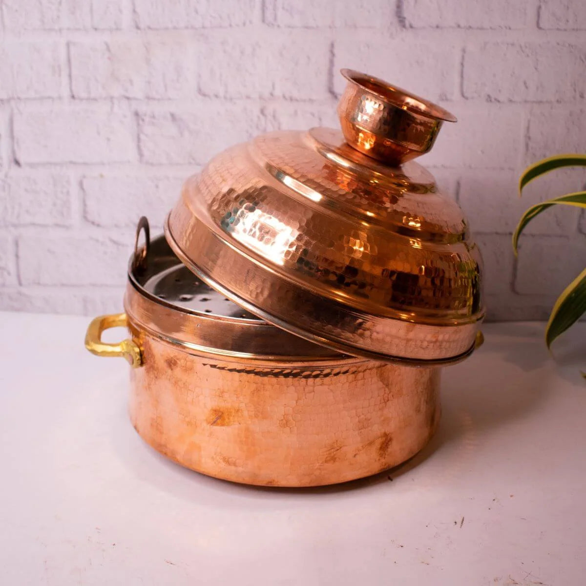 Copper Modak Patra with lid on a white surface against a white brick wall background-Zishta Traditional Cookware