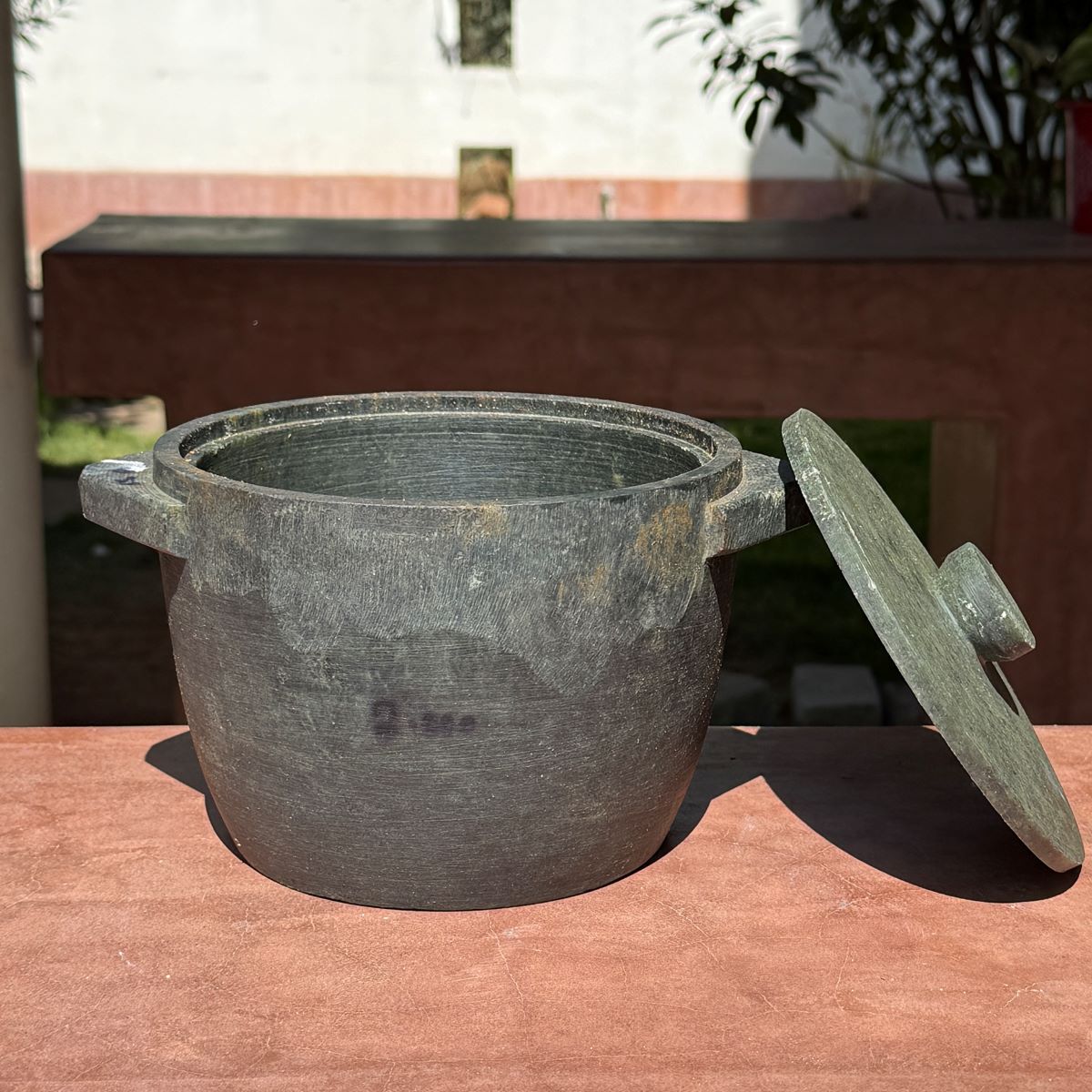 Treated Kalchatti-Soapstone pot with lid on a red surface outdoors-Zishta Traditional Cookware