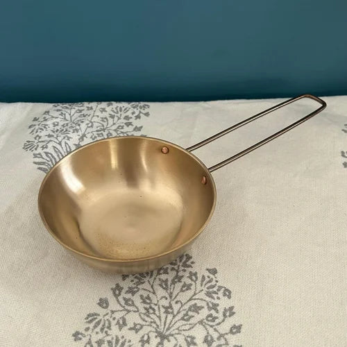 Bronze-Kansa Tulsi Tadka Pan with a handle on a patterned fabric background-Zishta Kitchen Accessories