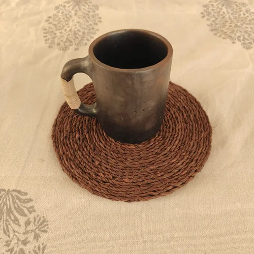 Manipur Black Pottery Milk Cup on a brown woven coaster with a floral-patterned fabric background-Zishta Traditional Serveware