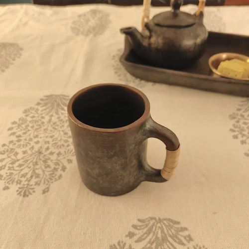 Manipur Black Pottery Milk Cup on a patterned tablecloth with a teapot in the background-Zishta Traditional Serveware