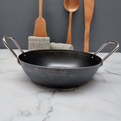 Pure Iron Flat Bottom Kadai with metal handles on a marble surface with wooden spoons in the background-Zishta Traditional Cookware