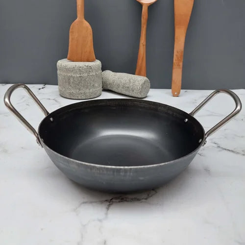 Pure Iron Flat Bottom Kadai with metal handles on a marble surface with wooden spatulas in the background-Zishta Traditional Cookware