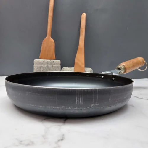 Iron frying pan with wooden handle and spatulas on a gray background-Zishta Traditional Cookware