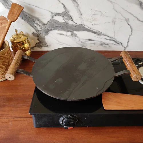 Pure Iron Round Tawa with Wooden handle on a hot plate with wooden spatulas and a marble backsplash-Zishta Traditional Cookware