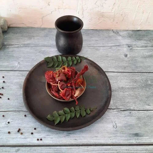 Dried red chilies on a Manipur Black Pottery Serving plate with a Black Pottery cup and leaves on a wooden surface-Zishta Traditional Serveware