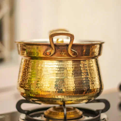 Brass Cooking Pot Shakuntala Patra on a stove with a blurred background-Zishta Traditional Cookware