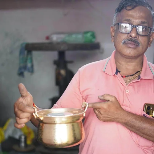 Artisan holding Shakuntala patra, a brass cooking pot in an indoor setting-Zishta Traditional Cookware