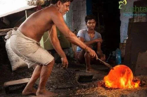 Two Artisans working with hot metal near a fire in an industrial setting making Iron Dosa Tawa-Zishta Traditional Cookware