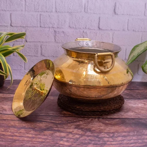 Brass Patili Handi-Cooking Pot with lid on a wooden surface against a white brick wall-Zishta Traditional Cookware