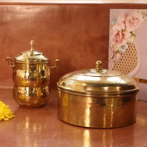 Brass Roti Box with Brass Ghee Pot in the back on a reflective surface with a floral card in the background-Zishta Traditional Kitchen Storage Containers