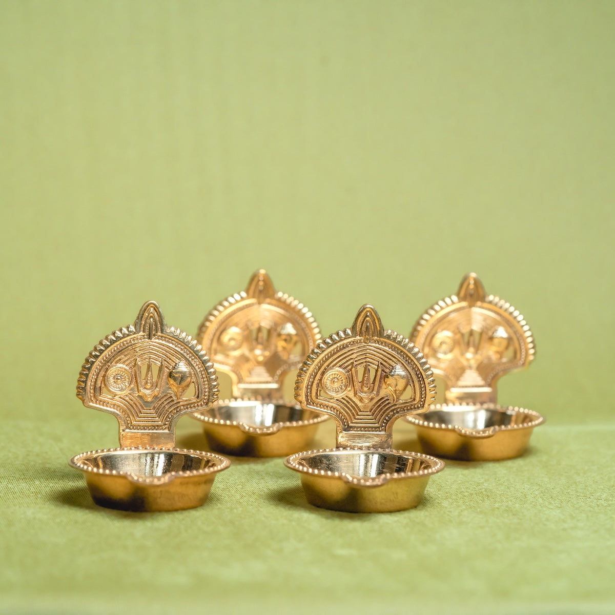 Set of four Handcrafted Brass Shankh Chakra Tilak Namah Diya oil lamps on a green background-Zishta Traditional Decor-Navratri Gifting