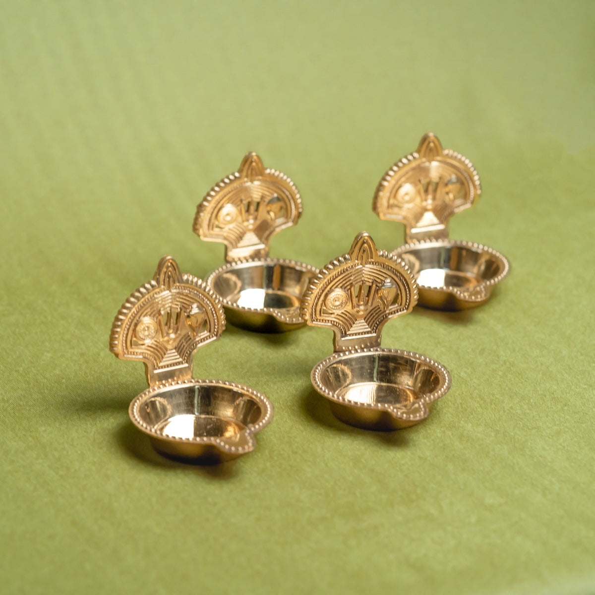 Set of four Brass Shankh Chakra Tilak Namah Diya oil lamps on a green background-Zishta Traditional Decor-Navratri Gifting