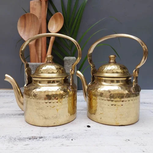 Two brass kettles on a wooden surface with wooden spoons and a plant in the background-Zishta Traditional Serveware