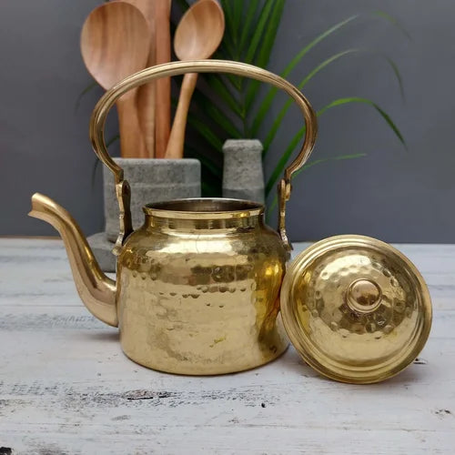 Brass teapot with lid on a wooden surface with kitchen utensils in the background-Zishta Traditional Serveware