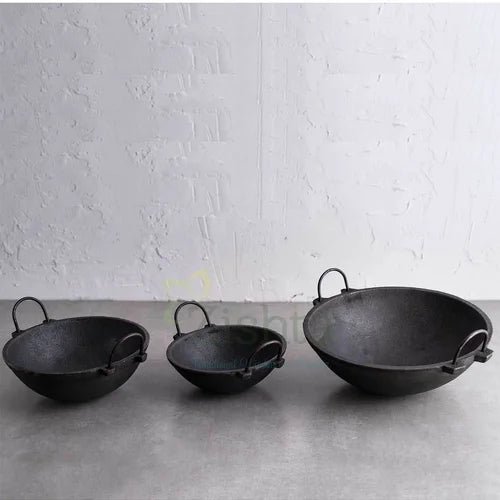 Three black cast iron kadais-medium,small and large sizes on a gray surface with a white textured wall background-Zishta Traditional Cookware