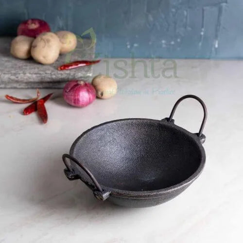 Cast iron kadai with handles on a white surface, surrounded by vegetables-Zishta Traditional Cookware