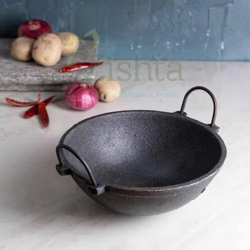 Black cast iron Kadai on a white surface with vegetables in the background-Zishta Traditional Cookware