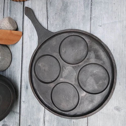 Cast iron mini uthappam pan with four circular depressions on a wooden surface-Zishta Traditional Cookware