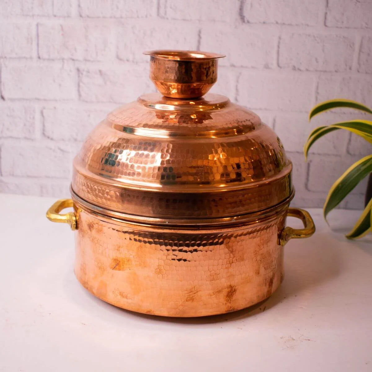 Copper Modak Patra with lid on a white surface against a white brick wall background-Zishta Traditional Cookware