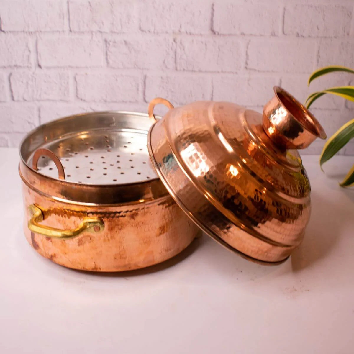 Copper Modak Patra with lid on a white surface with a light gray brick wall background-Zishta Traditional Cookware