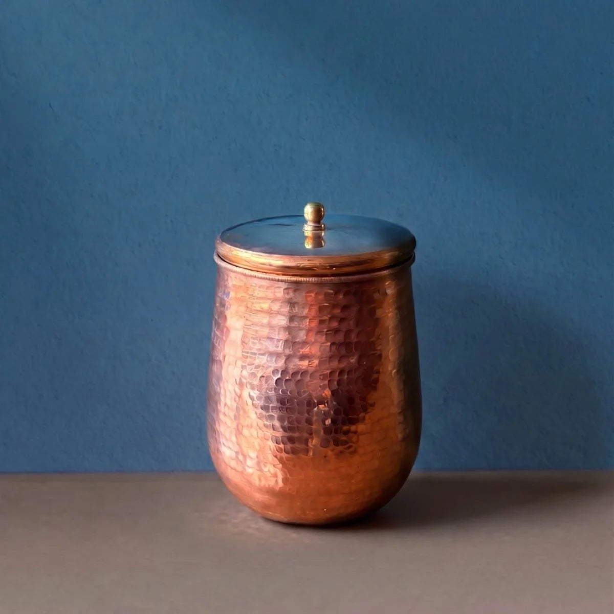 Copper glass with a lid on a blue background. Zishta Traditional Drinkware.