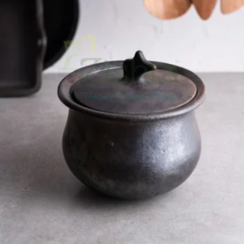Manipur Black Pottery Gravy pot  Hamlei with lid on a gray surface, with wooden spoons in the background-Zishta Traditional Cookware