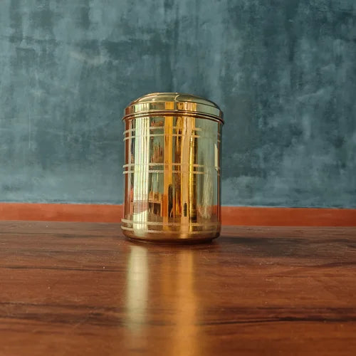 Brass Storage container on a wooden surface with a blue textured wall background-Zishta Traditional Storage Containers