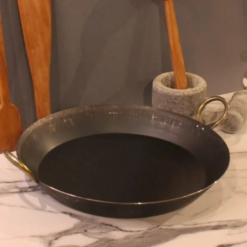 Zishta Paella Pan Flat Bottom Black frying pan on a marble surface with kitchen utensils in the background