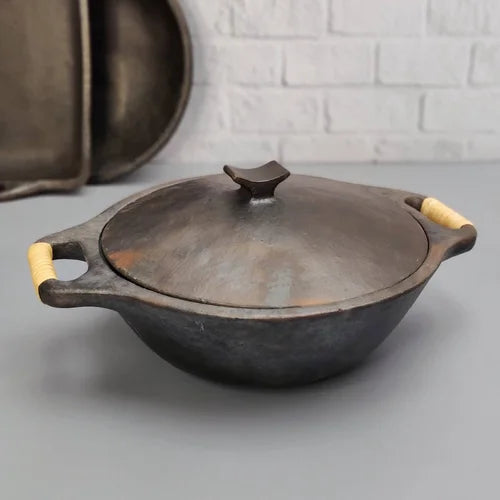 Manipur Longpi Black Pottery Kadai with wooden handles on a gray surface with a white brick wall background-Zishta Traditional Cookware