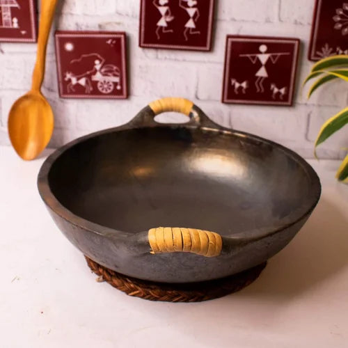 Manipur Black Pottery Open Kadai with wooden handle on a white surface, with decorative wall art in the background-Zishta Traditional Cookware