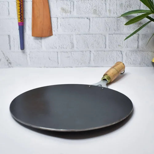 Pure Iron Roti Tawa with wooden handle on a white surface with a light gray brick wall background-Zishta Traditional Cookware
