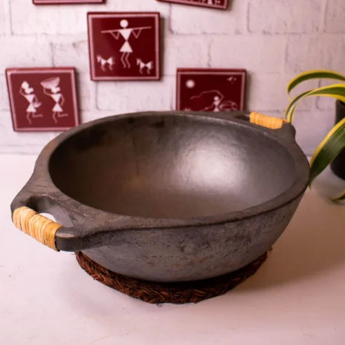 Manipur Longpi Black Pottery Wok with wooden handles on a white surface, with decorative wall art in the background-Zishta Traditional Cookware